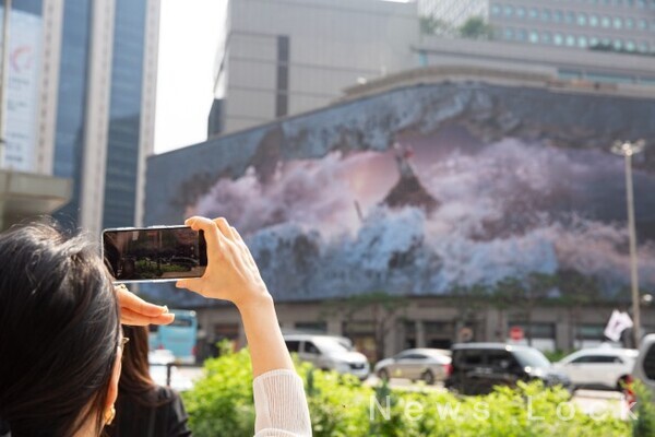 오는 11월 30일까지 명동 신세계 백화점 미디어월(신세계스퀘어)에서 공개되는 아트코리아랩  전시에서 시민과 관람객이 명진영, 이윤서 작가의 3D 아나모픽 미디어아트 작품 ‘불멸의 파도(Immortal Wave)’를 사진으로 담고 있다.